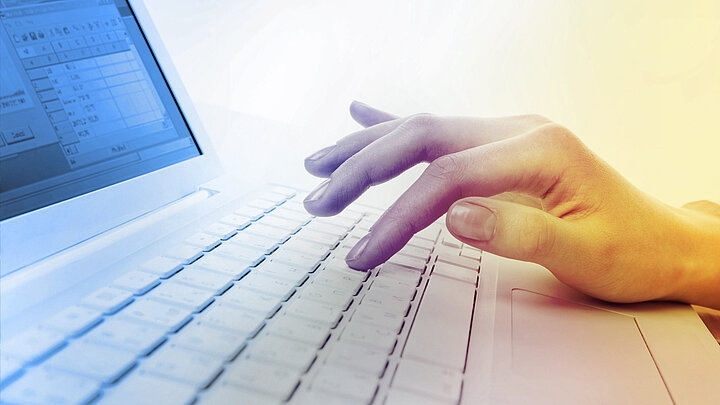Zdjęcie damskiej dłoni piszącej na klawiaturze laptopa.